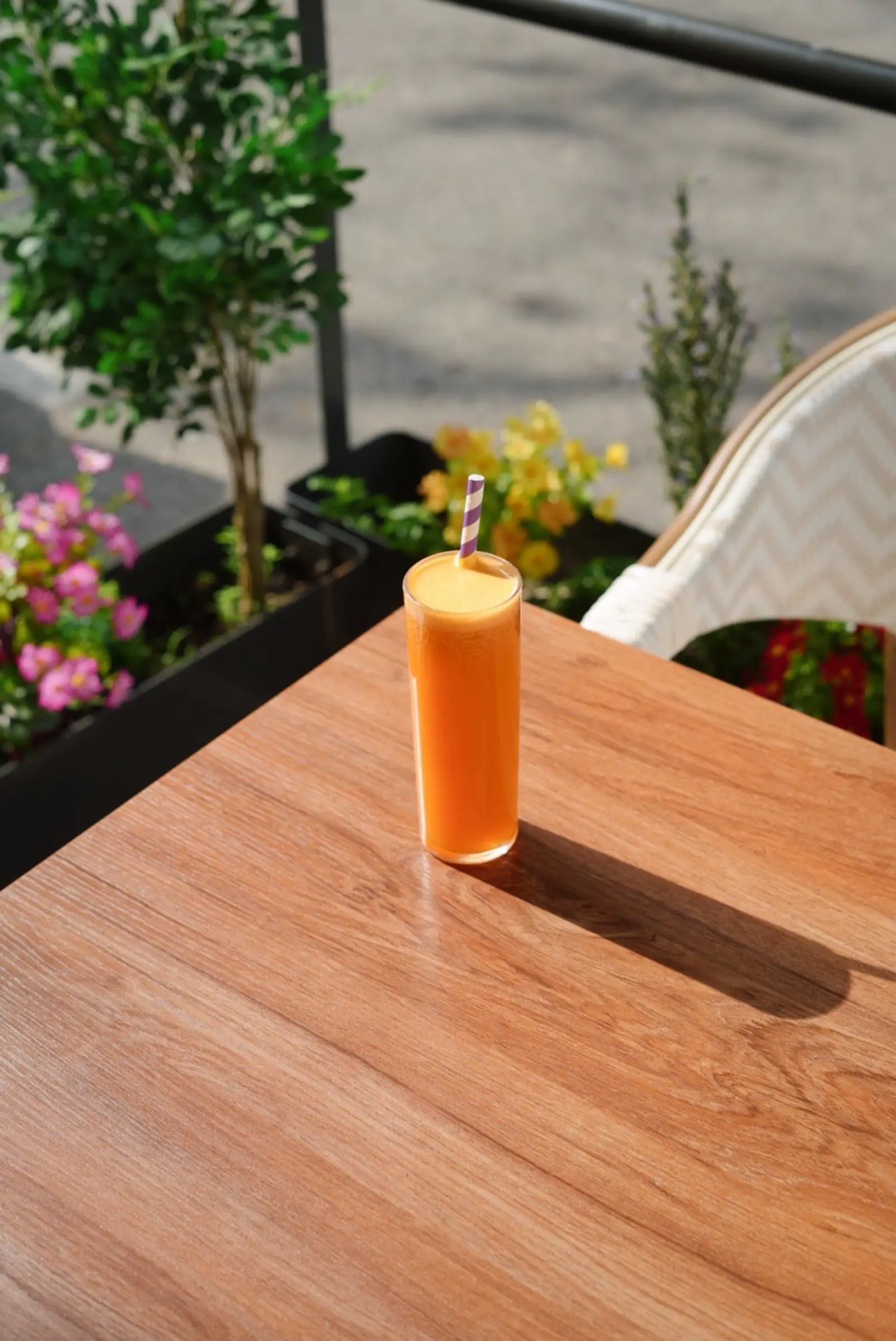 A fresh orange juice on a terrace table, with flowers in the planters
