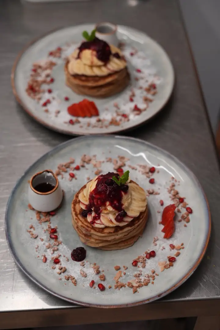 Two plates of pancakes topped with banana, berry compote and strawberries