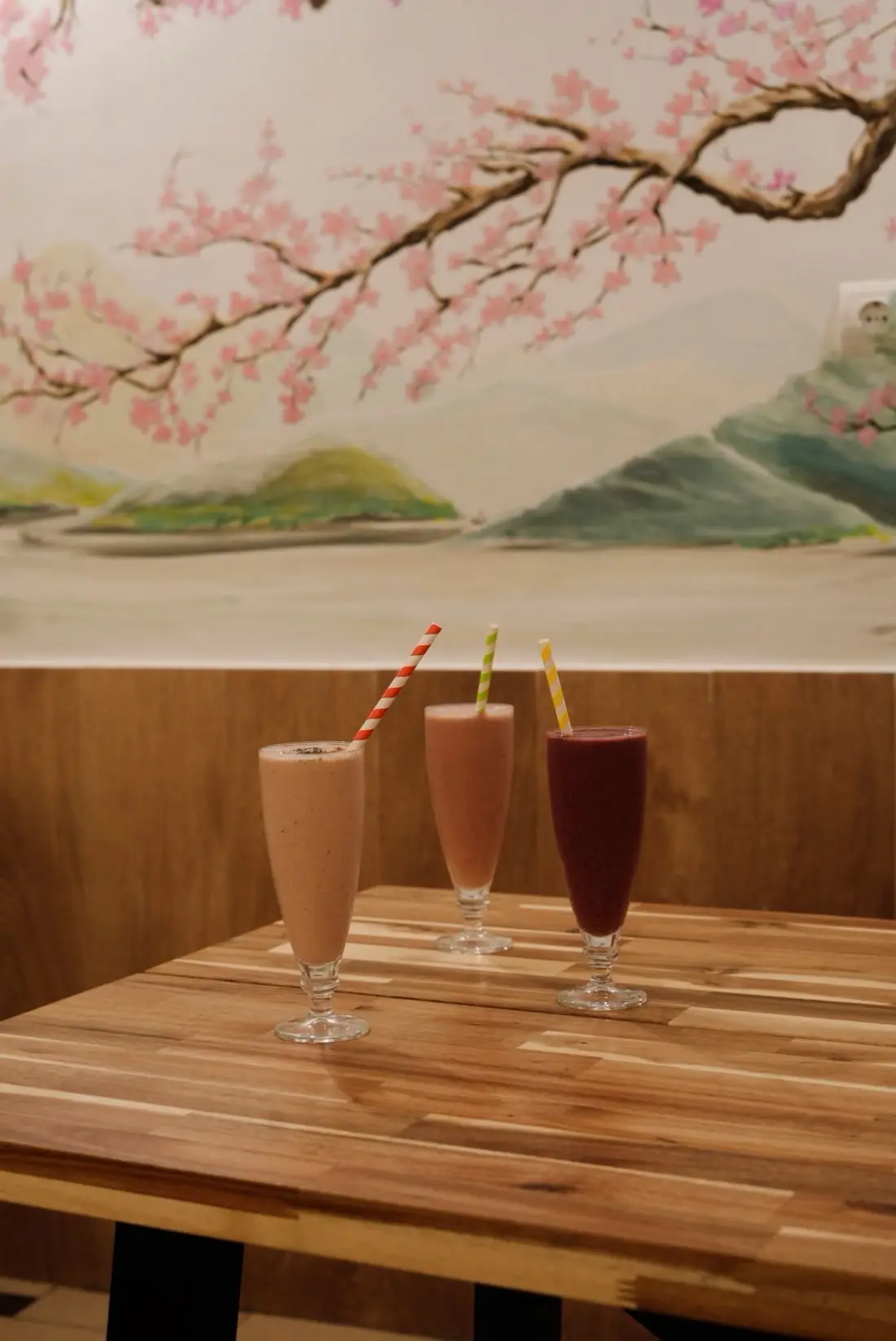 Three smoothies on a wooden table under the cherry blossom mural