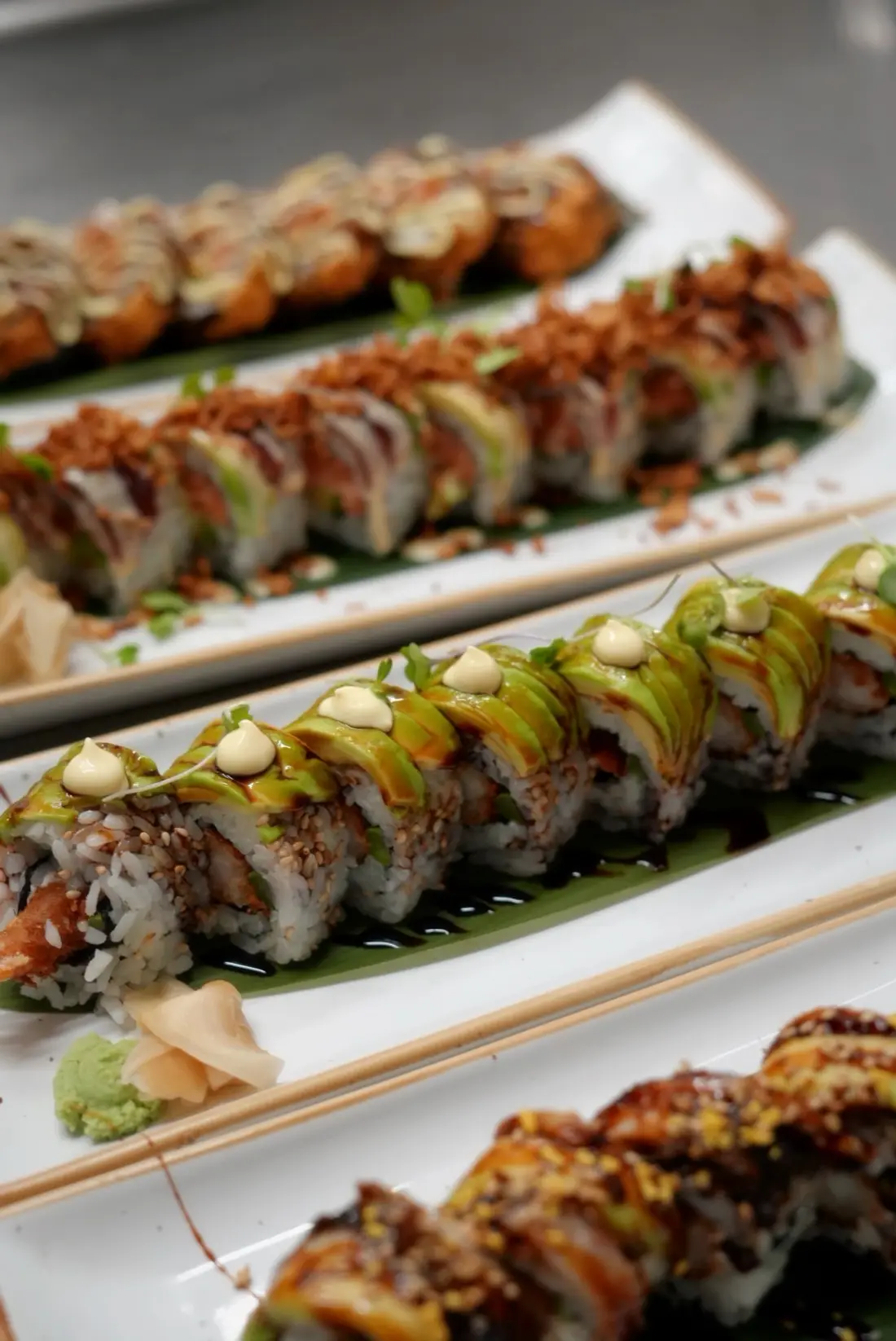 Sushi rolls topped with avocado, on long white plates