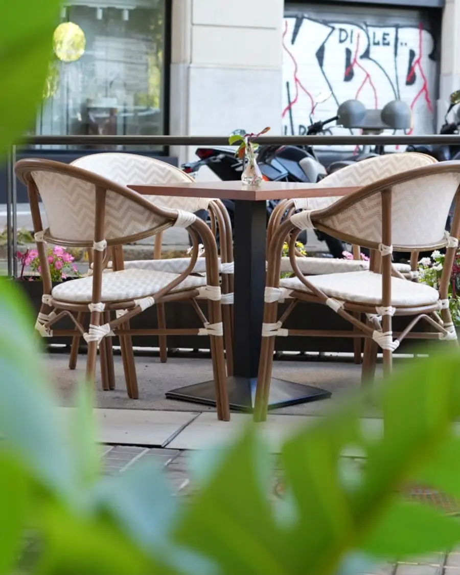 Rattan chairs on the street terrace, seen through leaves
